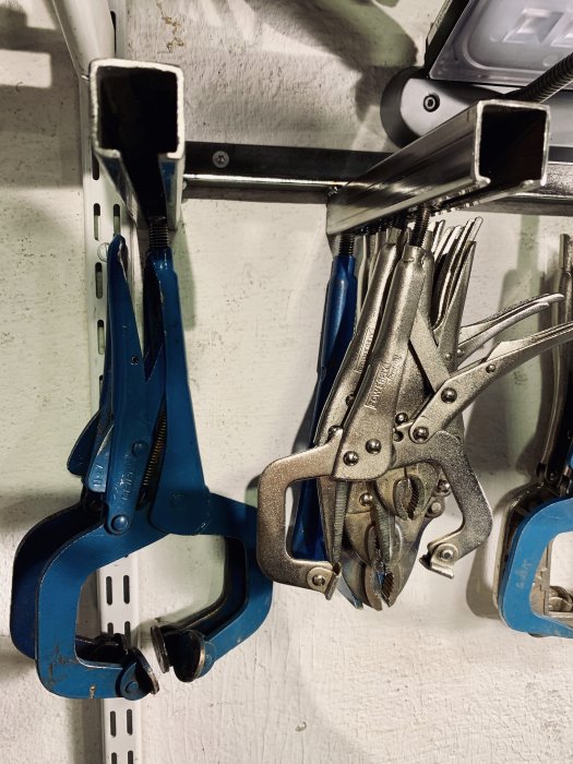 Svetstvingar och andra klämtänger hängande i ordning på en verktygstavla med justerskruvar för enkel förvaring.