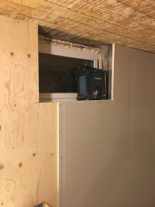 Renovering pågår med nytt fönster synligt, och vägg som delvis är täckt av plywood och gipsskiva.