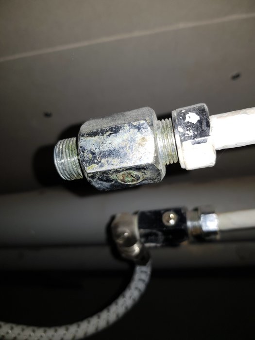 Närbild av två gamla rörkopplingar med en flexslang ansluten till den ena, belägna i taket.