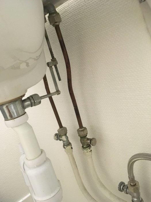 Vattenanslutning under handfat med kopparrör, avstängningsventiler och rördelar i behov av byte.