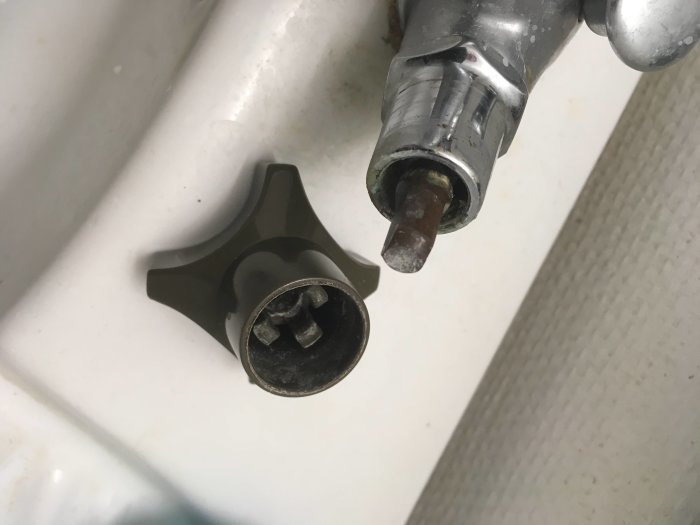 Närbild på en vattenkran och dess styrpinne framför ett vitt handfat.
