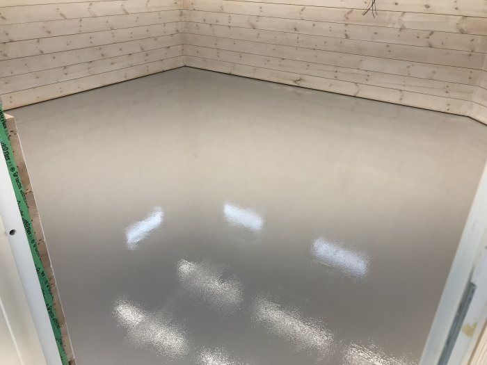 Nyutgjuten betonggolv i ett hörn av rum med träväggar, mätsticka syns till vänster.