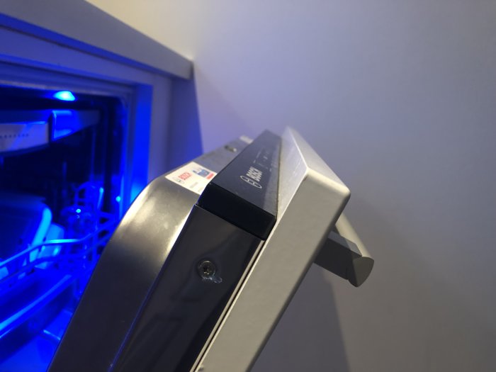 Närbild på en diskmaskins öppna dörr med blått ljus som lyser inifrån maskinen.