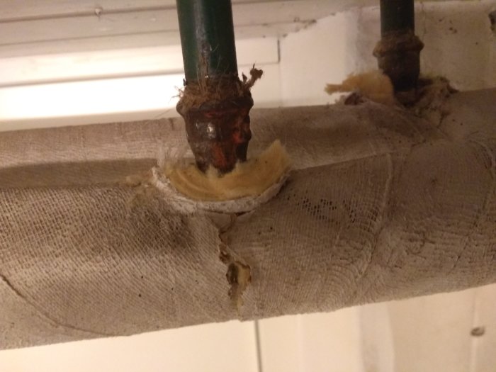 Avskalad isolering på T-kopplingar av värmeledningsrör med synligt vitt och gult material som ifrågasätts för asbestinnehåll.