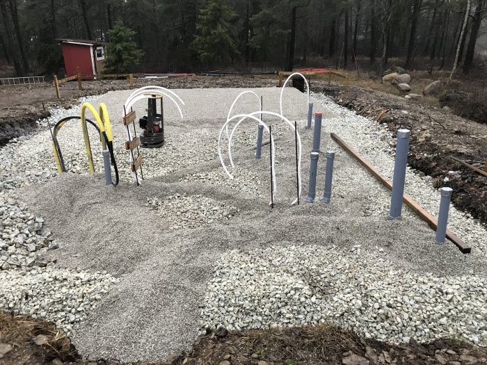 Grundarbete för hus med profiler för utstakning, avloppsrör och golvvärmeslangar på singelbädd.