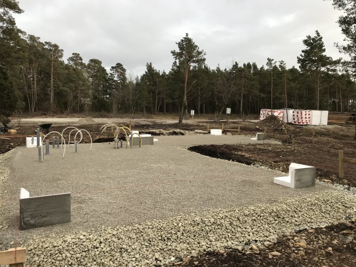 Byggplats med grus, kantelement och framstickande rör i början av ett byggprojekt.