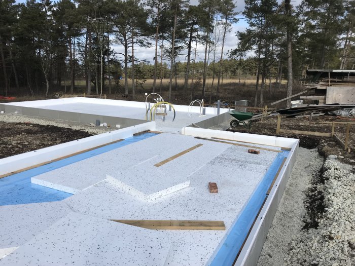 Grundarbete med kantelement och cellplast för isolering på en byggarbetsplats, med verktyg i förgrunden.