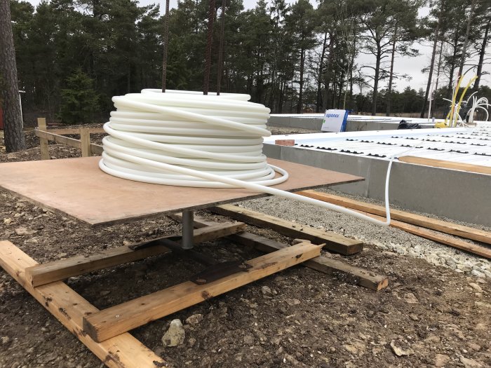 Golvvärmeslang på improviserad vinda bredvid grundplatta under arbete.