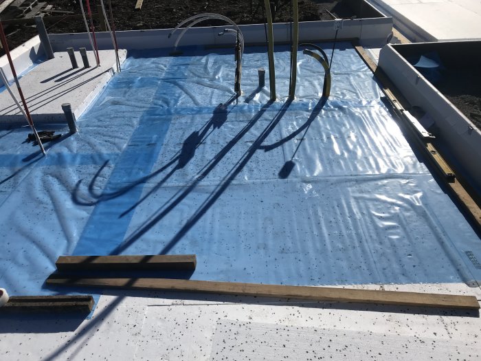 Byggarbetsplats med utlagd golvvärme över cellplastisolering och skyddande plastfilm.