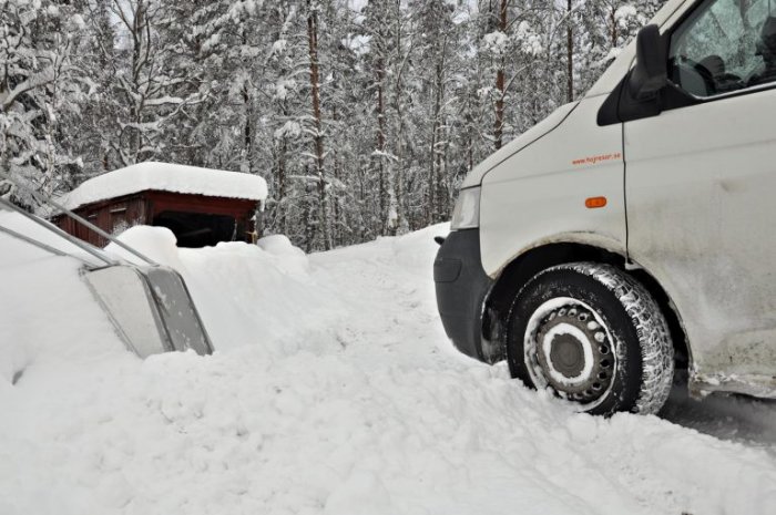 Vit Transporter-skåpbil parkerad i snödriva med skog i bakgrunden.