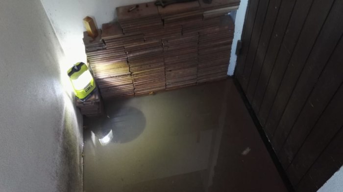 Översvämmad källare med vattenpump och skadade brädor upp till 30 cm på väggen.