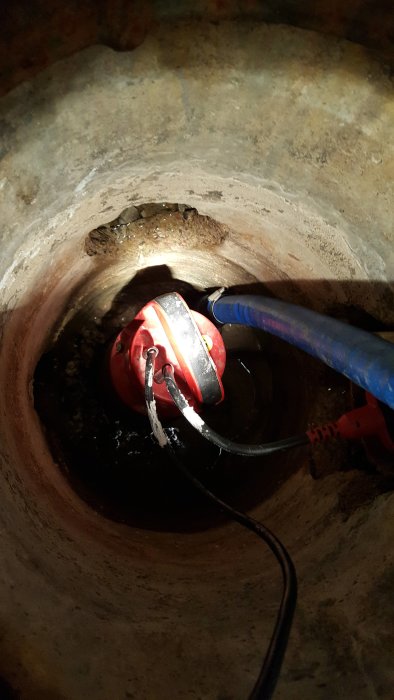 Pump i en översvämmad brunn i källaren för att evakuera vatten, omgiven av betong och sladdar.