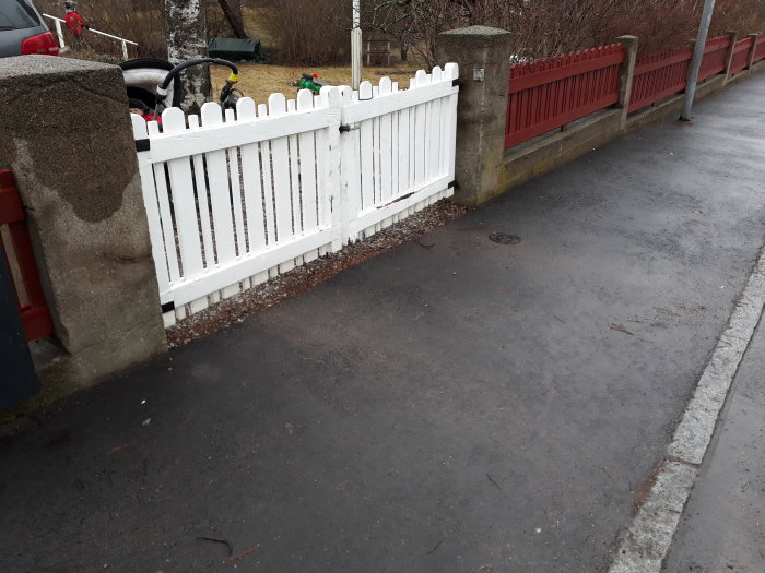 Vit trägrind vid infart med början av murknad, staket bakom i samma stil.