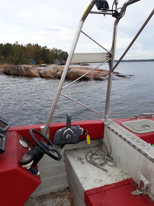 Ett inre hörn av en renoverad Crescent Bamse båt med rödmålade sidor och ny styrpulpet mot bakgrund av sjö och klippor.