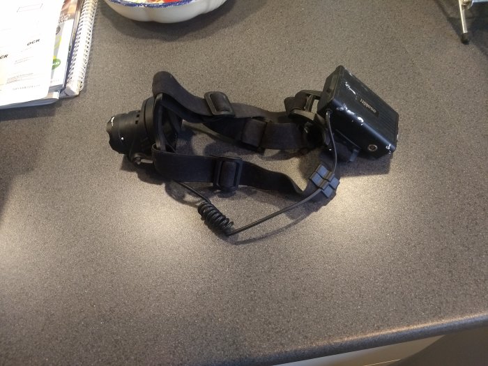 Asaklitt pannlampa med justerbara band och batteripack på ett köksbänkskiva.