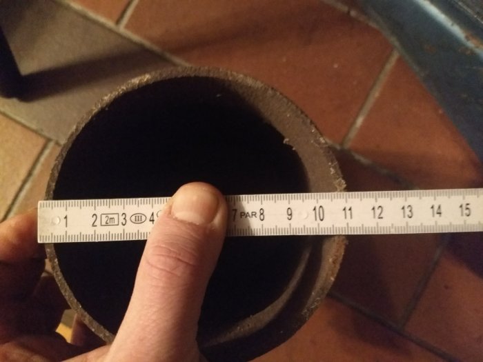 Hand håller måttband vid ett bastant gjutjärnsrör för att mäta diametern.