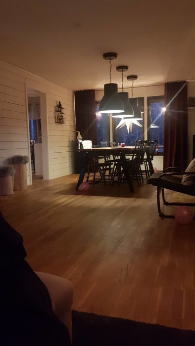 Matrum med parkettgolv, brädvägg och matbord under upphängd stjärnformad lampa.