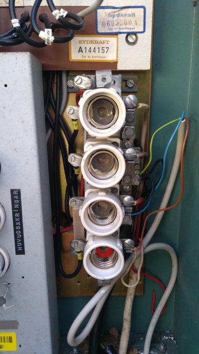 Gammal elinstallation med säkringar, blandade flätade och nyare kablar i plintar, i ett äldre hus.