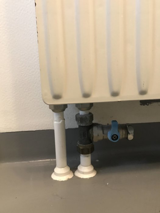 Vattenburen radiator ansluten till vitmålade rör och termostatventil i ett tvårörssystem.
