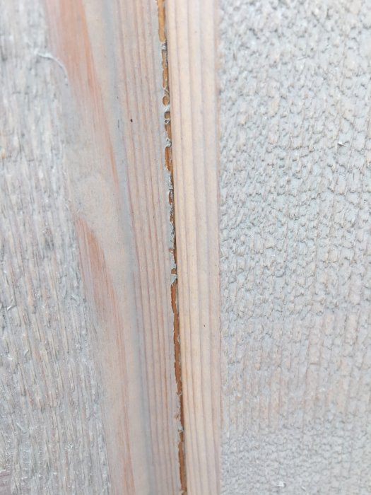 Närbild på en stående spontad panel med synlig krympning och obehandlat trä mellan målade ytor.