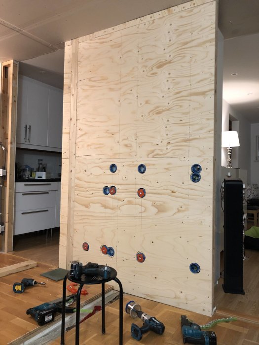 Plywoodvägg förberedd för TV-montering med förstärkning och synlig regel, verktyg i förgrunden.