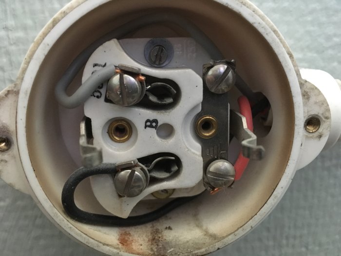 En närbild på en öppnad elektrisk uttag med exponerade kablar; svart och grå kopplade till terminaler.