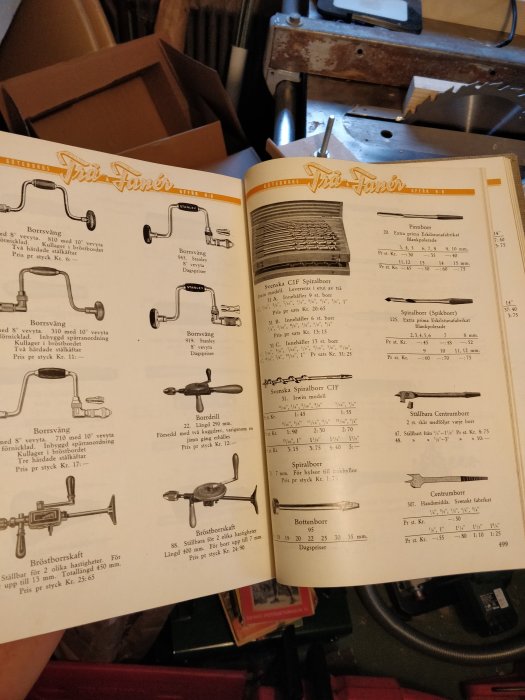 Öppen verktygskatalog med bilder av äldre handverktyg och beskrivningar på svenska, framför verktygslådor.
