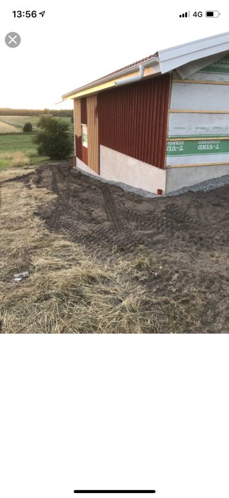 Utgrävning vid husvägg med gruslag för leca-block framför dörr, gräsmark och öppet fält i bakgrunden.