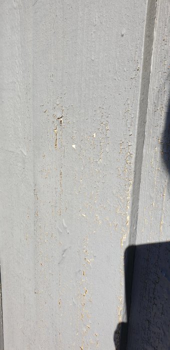 Fasad med avflagande grå färg och synligt träverk på ett hus utsatt för solslitage.