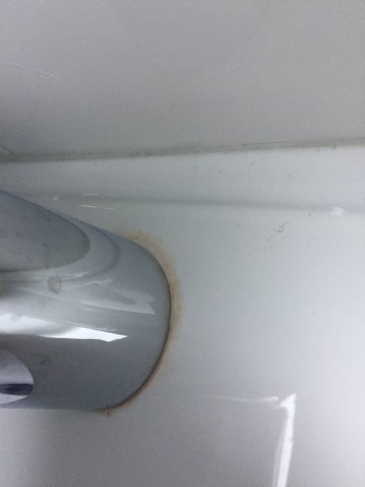 Brunt märke på handfatet runt basen av en tvättställsblandare.