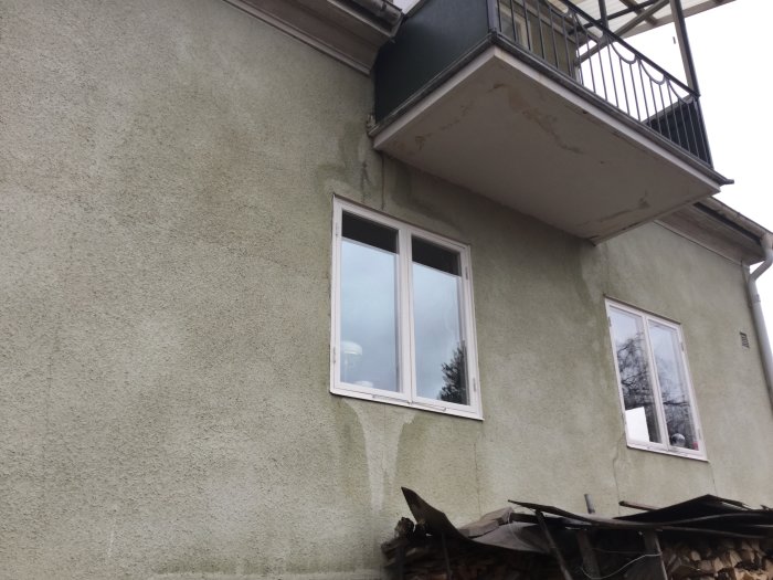 Blekt putsfasad med småsprickor på ett 1,5-plans hus från 30-talet, behöver underhåll.