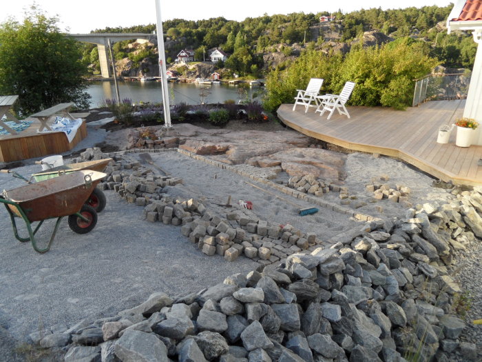 Upprivning av smågatsten från garageuppfart med skottkärra och verktyg i förgrunden.