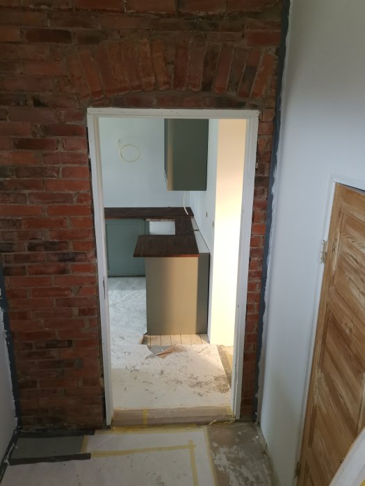 Öppning med vit dörrkarm i en tegelvägg som leder till annat rum under renovering, fråga om bärande funktion.