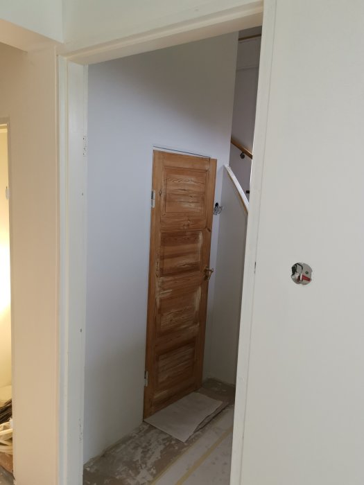 Öppen träddörr i en tom vitmålad dörrkarm i en under renovering interiör.