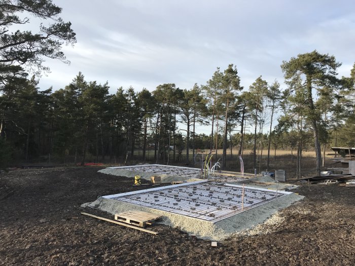 Armerad betonggrund klar för gjutning med armeringsnät, grus och gjutformar på en byggarbetsplats.