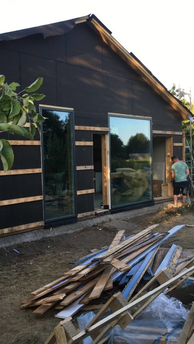 Person som mäter på stort fönster under installation på ett hus under renovering, med byggmaterial i förgrunden.