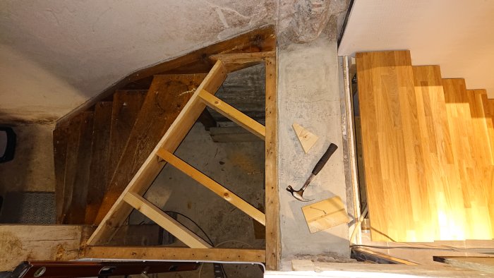 Pågående renovering av en trappa med trästeg, verktyg och en ojämn betongklack synlig.