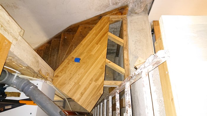 Pågående konstruktion av en trätrappa med synliga stödbjälkar och en betongklack i ett hem under renovering.