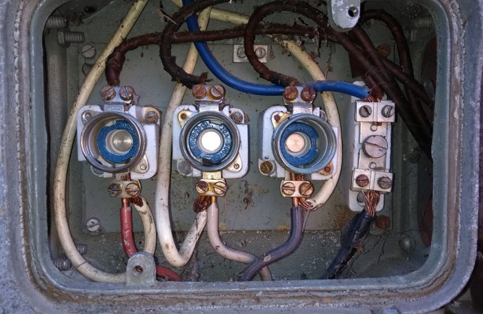 En öppen elektrisk säkringslåda med synliga kablar och kopplingar, tecken på åldring och korrosion.