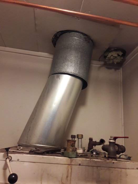 Äldre panna med isolerad röranslutning och kopparledningar i ett pannrum.