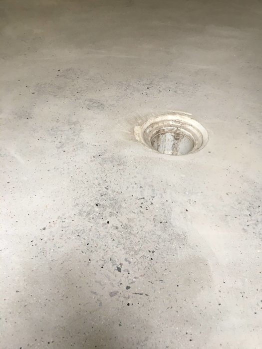 Partially sanded concrete floor with visible layers and a central floor drain.
