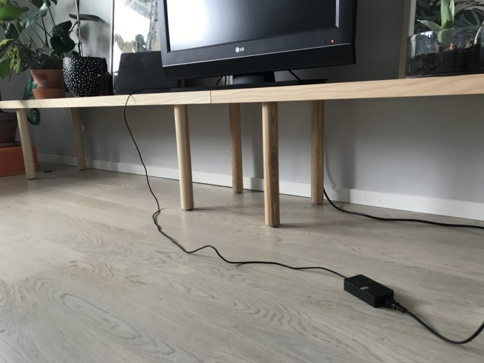 Nytt parkettgolv med synlig glipa vid fotlisten under ett TV-bord i ett vardagsrum.