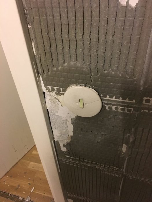 Vägg med gammalt kakelfix och en synlig lättbetongstruktur, med en delvis exponerad yta och eluttag.