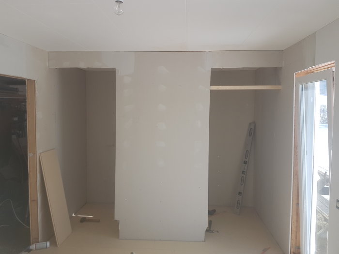 Renoveringsrum med nysatt spackel och en installerad skjutdörr, andra dörren och väggar ej klara.