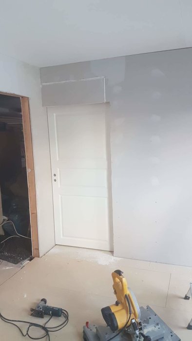 Nyinstallerad vit skjutdörr i ett rum under renovering med nyspacklade väggar och verktyg på golvet.