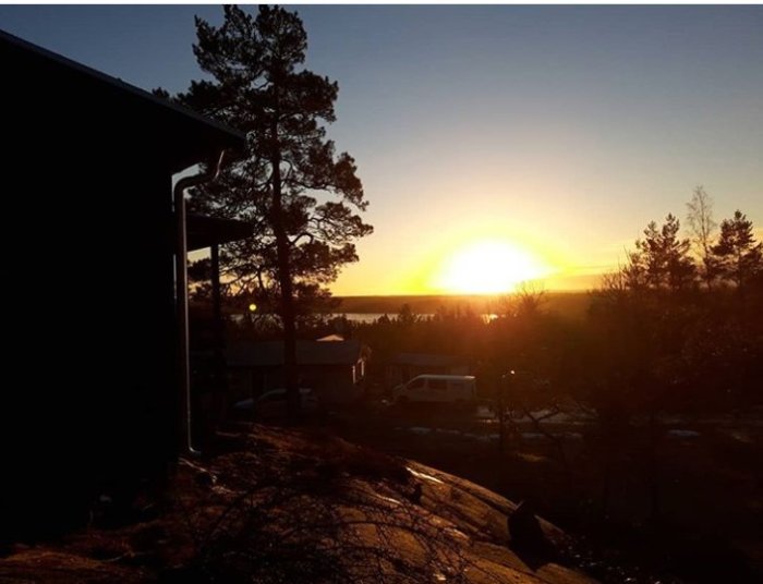 Solnedgång över en sluttande bergstomt med träd och en byggnads siluett.