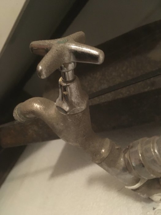 Närbild av en äldre vattenkran med ett kryssformat handtag som visar tecken på kalkavlagringar och slitage.
