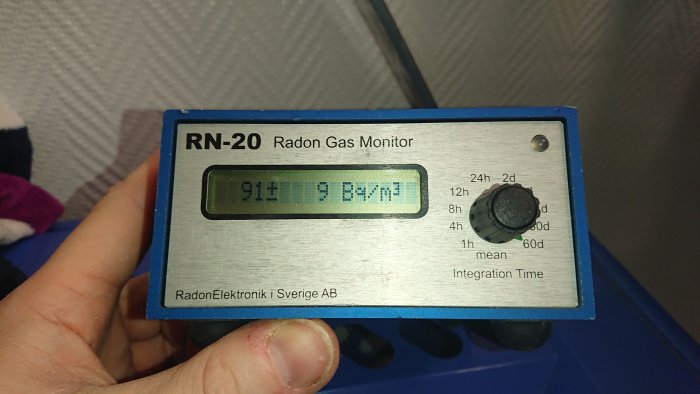 Radonmätare RN-20 visar radonvärde 91 Bq/m³ på digital display, handhållen av person.