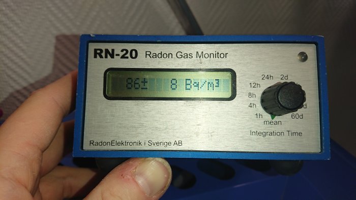 Hand håller en RN-20 Radon Gas Monitor som visar radonvärde på skärmen.