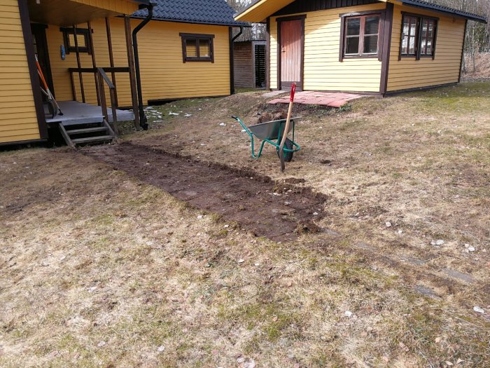 En nyligen frilagd stenlagd gång mellan gulmålade hus med en skottkärra och uppgrävd mark.